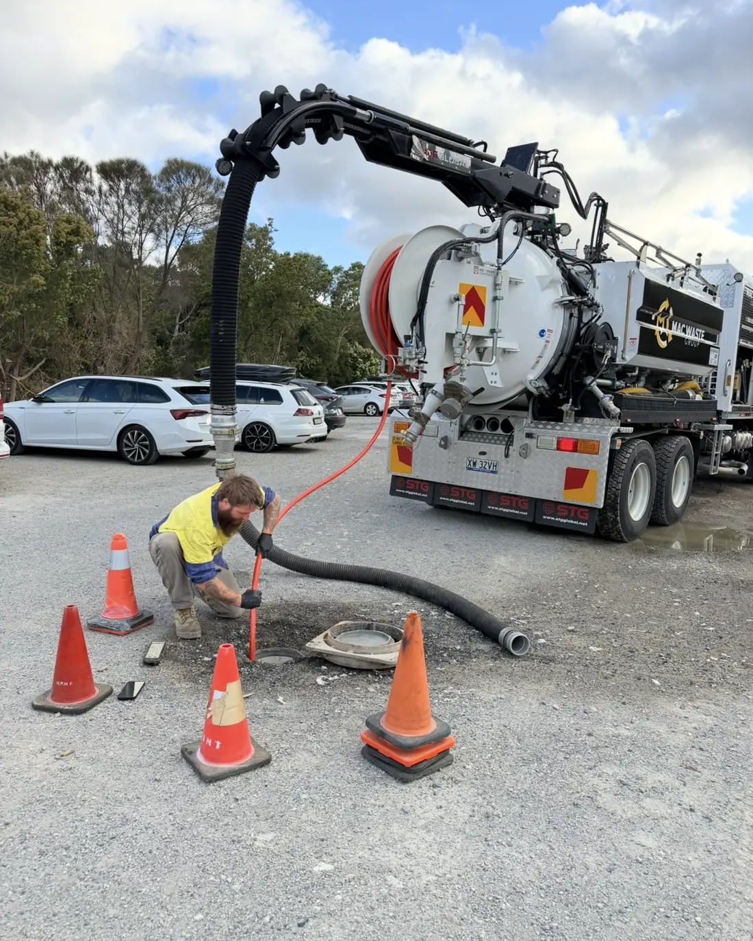 Mac Waste operator running a suction hose into a pit with traffic cones set out around the job